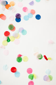 Colorful paper confetti scattered across a bright white background, creating a festive and playful composition. The image features vibrant multicolored paper circles with ample copy space