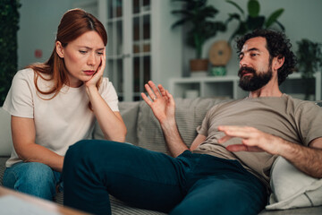 Fototapeta premium Couple discussing relationship problems at home, woman looking unhappy, man explaining disagreement