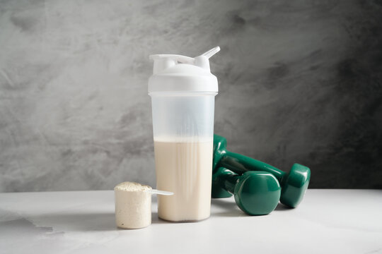 Protein powder and shaker bottle with workout gear on gray background, copy space