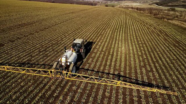 Agricultural tractor spraying crops in a vast field, showcasing the continuous action of crop treatment with visible rows of plants and farmland in the background