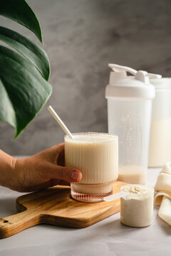 Hand holding protein shake glass with whey powder scoop, sports nutrition concept