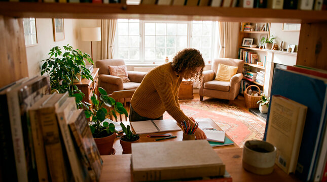 Woman organizing study books and desk in cozy sunlit home library