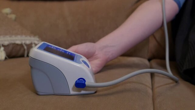 Individual holding portable blood pressure cuff device while taking vital signs reading at home for health monitoring, wellness, medical check.