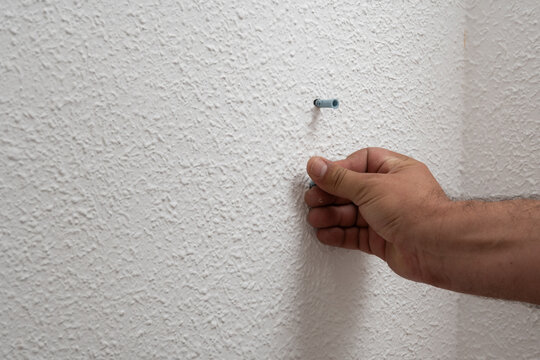Hand installing wall anchor into textured white wall