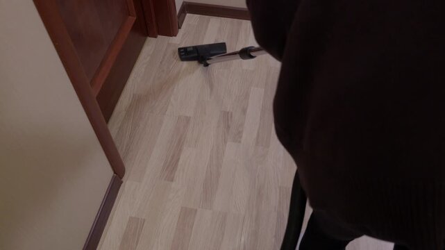 Robotic vacuum cleaning device moves across light wood laminate flooring in residential hallway with brown wooden doors, demonstrating automated floor cleaning technology.
