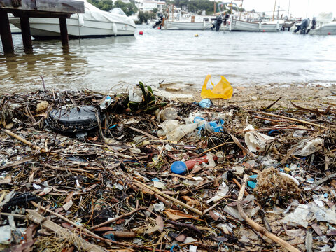 Plastic rubbish and assorted waste washed up at waters edge in harbour in Spain, whilst smart expensive yachts are moored nearby. Pollution from tourism damages the environment.