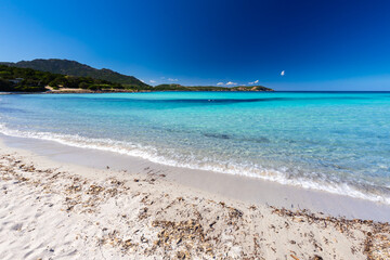 Obraz premium Rocky-sandy coastline with turquoise sea, white sand beach and blue sky in Sardinia, Costa Smeralda, Grande Pevero Beach, Italy - background or travel wallpaper 