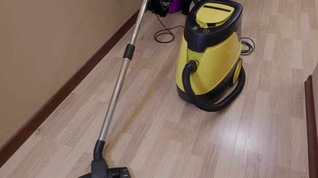 Worker begins using yellow and black steam cleaning machine on light wood flooring indoors. Professional cleaning equipment in action on residential surface.