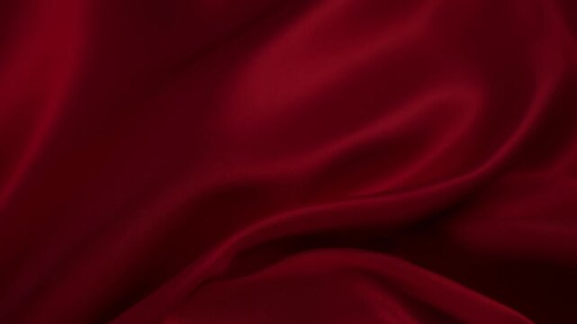 Slow motion static close up of red satin fabric billowing and folding over dark studio backdrop, glossy drape texture and gentle rippling movement