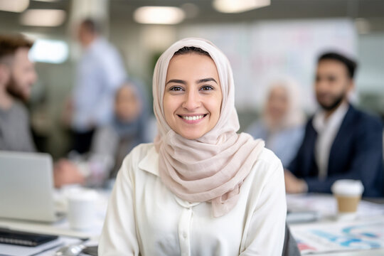 Happy Muslim Woman Smiling at Camera in Modern Office With Colleagues in Background, Professional Workplace Portrait Showcasing Confidence, Diversity, Career Success and Positive Team Environment