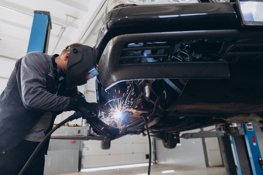 Auto mechanic welding car parts in service garage
