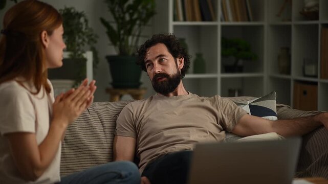 Frustrated couple having a difficult conversation and arguing on the sofa in the living room during the evening