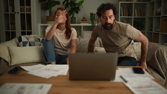 Stressed couple arguing over finances, bills, and debt while sitting on the sofa at home, facing relationship problems
