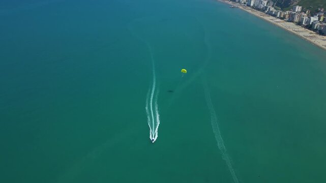 Top Down Aerial Shot Tracking a Speedboat and Yellow Parasailer Gliding Across the Turquoise Sea