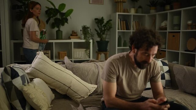 Frustrated woman arguing with her boyfriend who is ignoring her and using his smartphone on the sofa at home