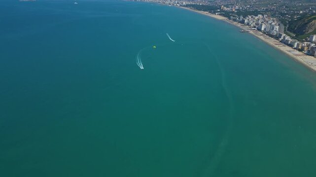 High Altitude Aerial Shot of a Speedboat Pulling a Yellow Parasailer Along the Coastal Beachline