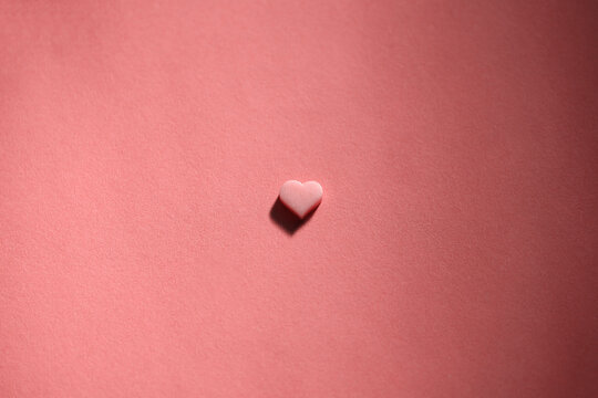 Tiny heart shaped chocolate on matching color background, flat lay
