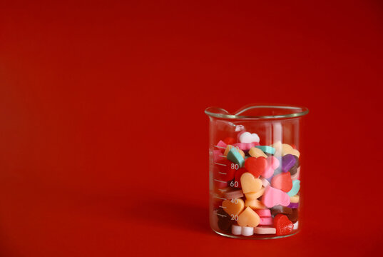 Colorful heart shaped chocolates in a glass beaker on a solid background
