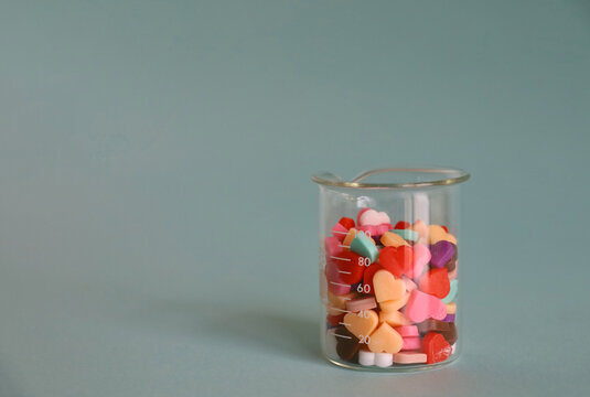 Colorful heart shaped chocolates in a glass beaker on a solid background
