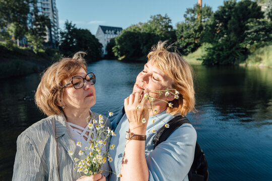 Happy Senior Women Sharing Warm Moment With Chamomile Flowers Near City Waterfront