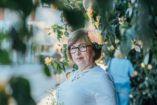 Thoughtful Senior Woman Framed By Blooming Roses During Peaceful Summer Evening Walk