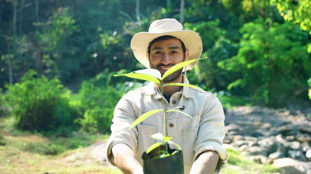 Portrait of a smiling man holding a young tree sapling in a biodegradable planting bag outdoors. Environmental conservation, reforestation, sustainability, climate action, and ecological responsibilit
