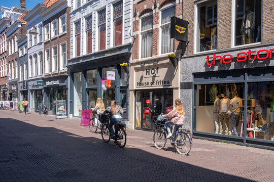 Cyclists riding sunny brick shopping street in historic Delft city center, Netherlands