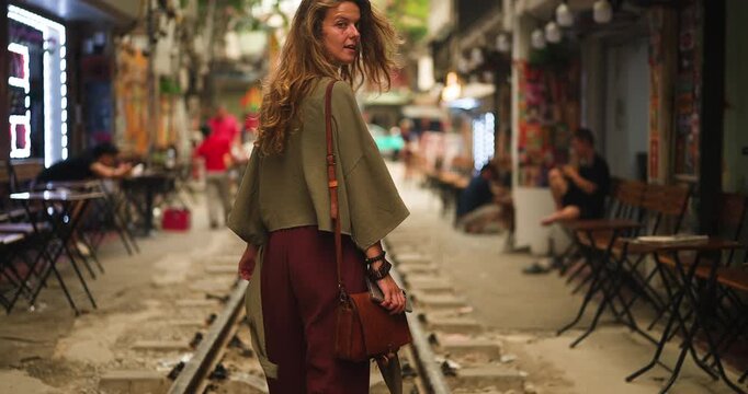 A young woman with beautiful curly hair walks along the famous Train Street in Ha Noi, Vietnam, taking in the unique urban atmosphere and local culture.