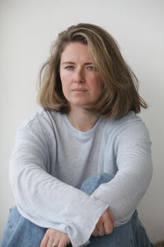 Portrait of an authentic midlife woman with an sad, thoughtful expression indoors on neutral background. Concepts of life experience, self reflection, personal growth, emotional wellbeing, stress.
