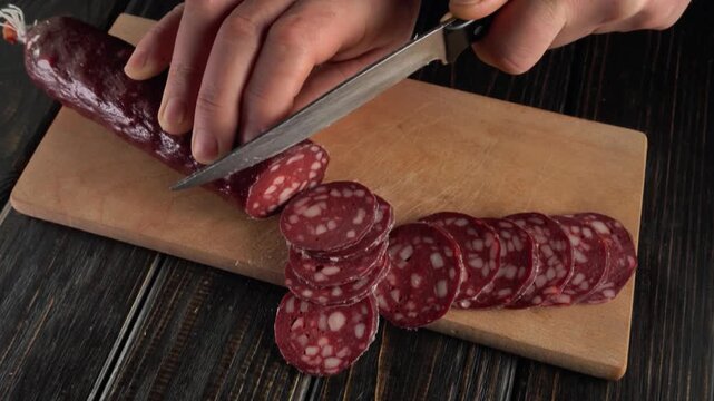 Hands slicing sausage into thin rounds on a wooden cutting board, showcasing the process of preparing meat for a dish in a kitchen setting