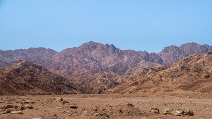 Fototapeta premium Scenic view of a desert landscape with rugged rocky mountains and a highway road under a clear blue sky.