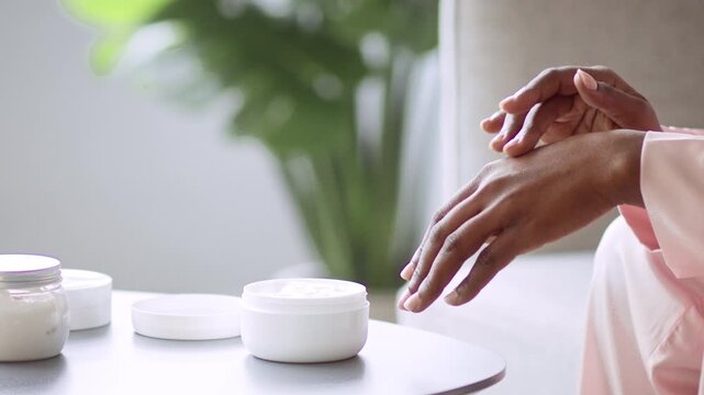 Focused Woman Applying Moisturizer On Hand While Sitting In Bright Room With Natural Light. Emphasizing Daily Skincare Routine To Maintain Healthy Skin At Home, Wellness Concept.