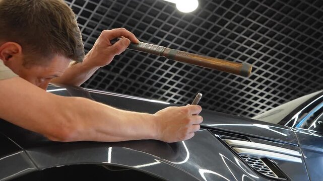 PDR. Paintless Car Dent Repair. Process of paintless dent repair on car body. The mechanic at the auto shop with tools to repair dents in car body. Body repair. A specialist repairs a dent on the car.