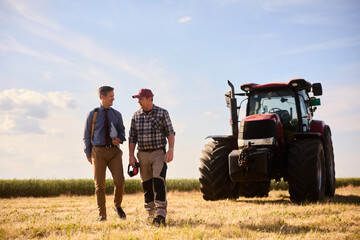Full length of agriculturist and bank manager communicating in field. © Drazen