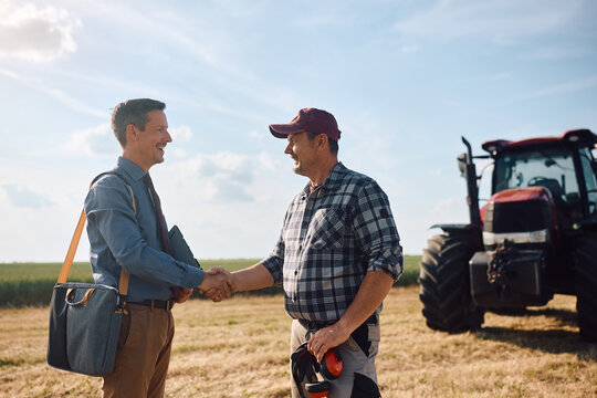 Happy farmer handshaking with insurance agent in field.