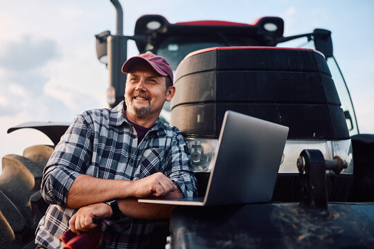 Happy farm worker using laptop while working in field.
