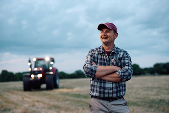 Successful agronomist standing with crossed arms in field and looking away.