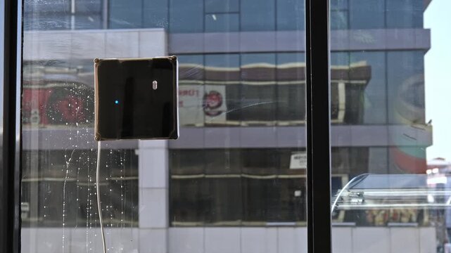 Robotic window cleaner attached to modern office glass, washing an urban building facade with city reflections, representing automation, hygiene, smart technology, and maintenance.