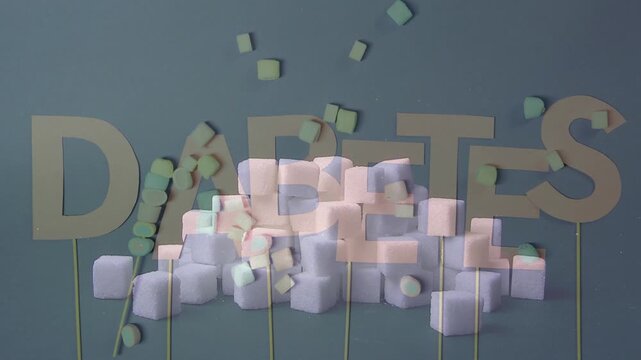 Cardboard letters spelling DIABETES surrounded by a pile of white sugar cubes and small colorful candies. High sugar intake health warning.
