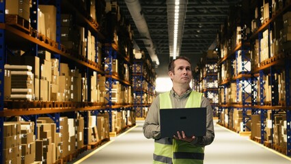 Fototapeta premium Warehouse staff member in facility checking pallets and packages, monitoring distribution on laptop, inventory tracking and workflow planning improve.
