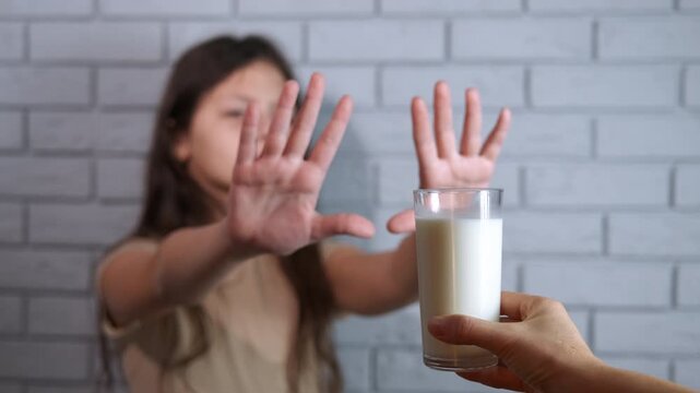 Child with lactose intolerance refusing a glass of milk. Young girl with a dairy allergy or lactose intolerance showing a stop gesture with her hands and refusing to drink a glass of milk