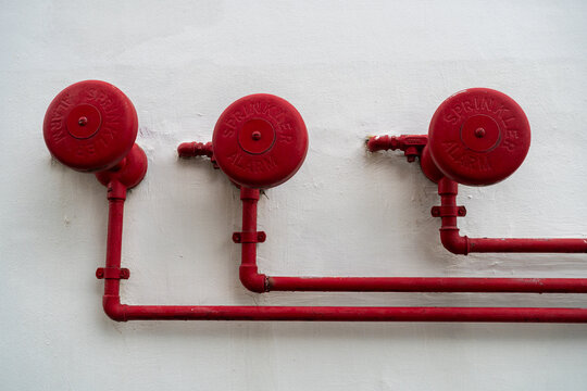 red fire alarm bells mounted on white wall with connecting pipes in industrial setting