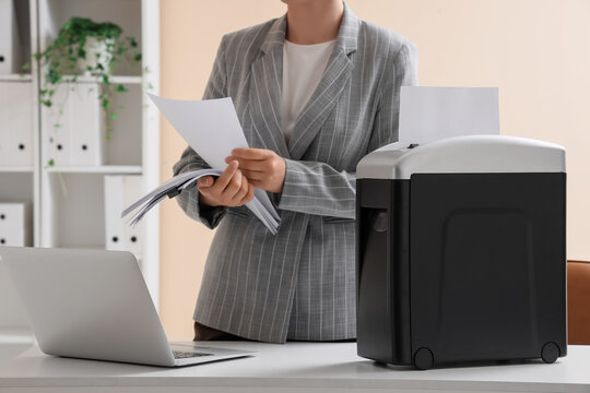 Businesswoman shredding confidential documents for data protection and information security in modern office, this action ensures the secure disposal of sensitive information