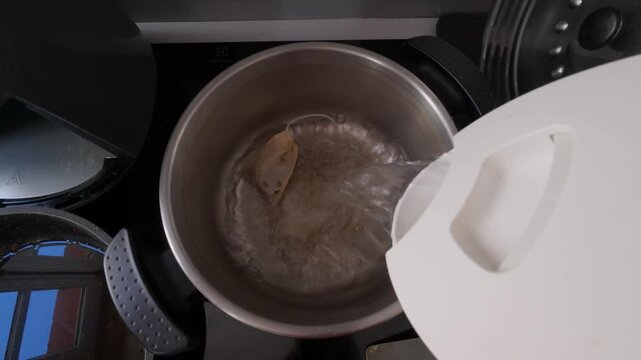 Water pouring from white kettle into metal pot with tea bag food preparation