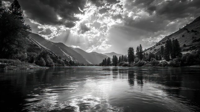 River scene with mountain backdrop. Dramatic sky casts light rays. Black & white landscape