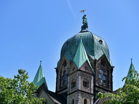  A low-angle shot focusing 
on the majestic green oxidized copper 
dome and spires of a historic cathedral. 
The central dome features detailed 
masonry, arched windows, and is 
topped with a green st