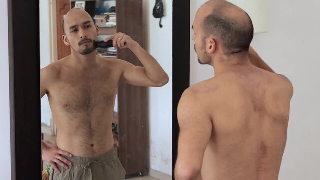 Young man grooming beard in mirror at home