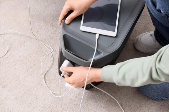 Person plugging charger into portable power station with tablet charging on top, modern energy solution, this modern energy solution provides convenient electricity for electronic devices