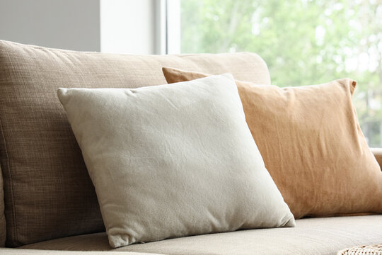 Comfortable beige and white throw pillows on a modern sofa in a bright living room interior, the neutral color palette complements the bright living room interior, with natural light streaming