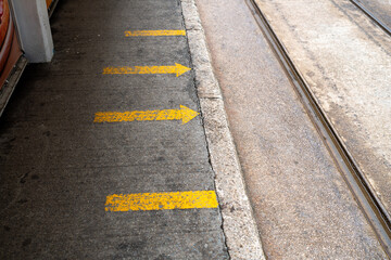 Obraz premium Yellow directional arrows painted on sidewalk at tram station platform next to tracks